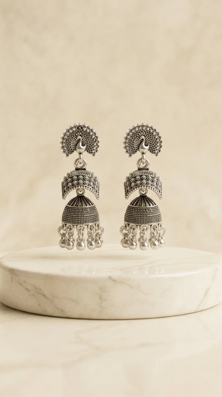 Oxidized silver peacock jhumka earrings on marble pedestal