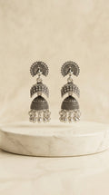 Oxidized silver peacock jhumka earrings on marble pedestal