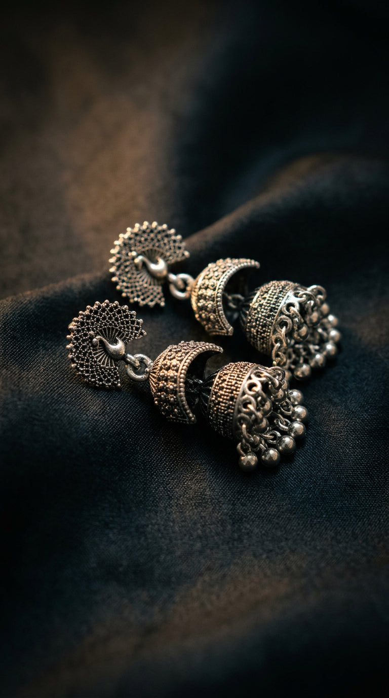 Close-up of peacock jhumka earrings on dark silk